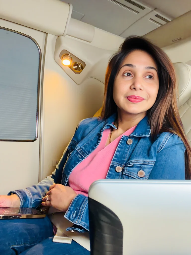 Preeti Mallapurkar wearing a pink dress with a stylish blue jacket over it while she is travelling in airplane.
