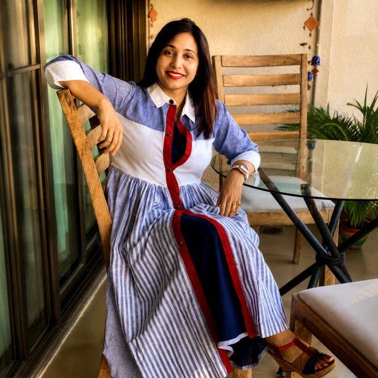 Marathi actress Preeti Mallapurkar sitting on a wooden chair with one hand resting on the back of the chair with a charming smile and in a beautiful dress.